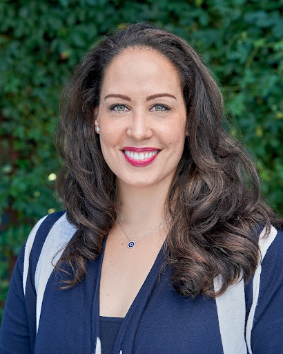 A woman smiling in front of bushes.