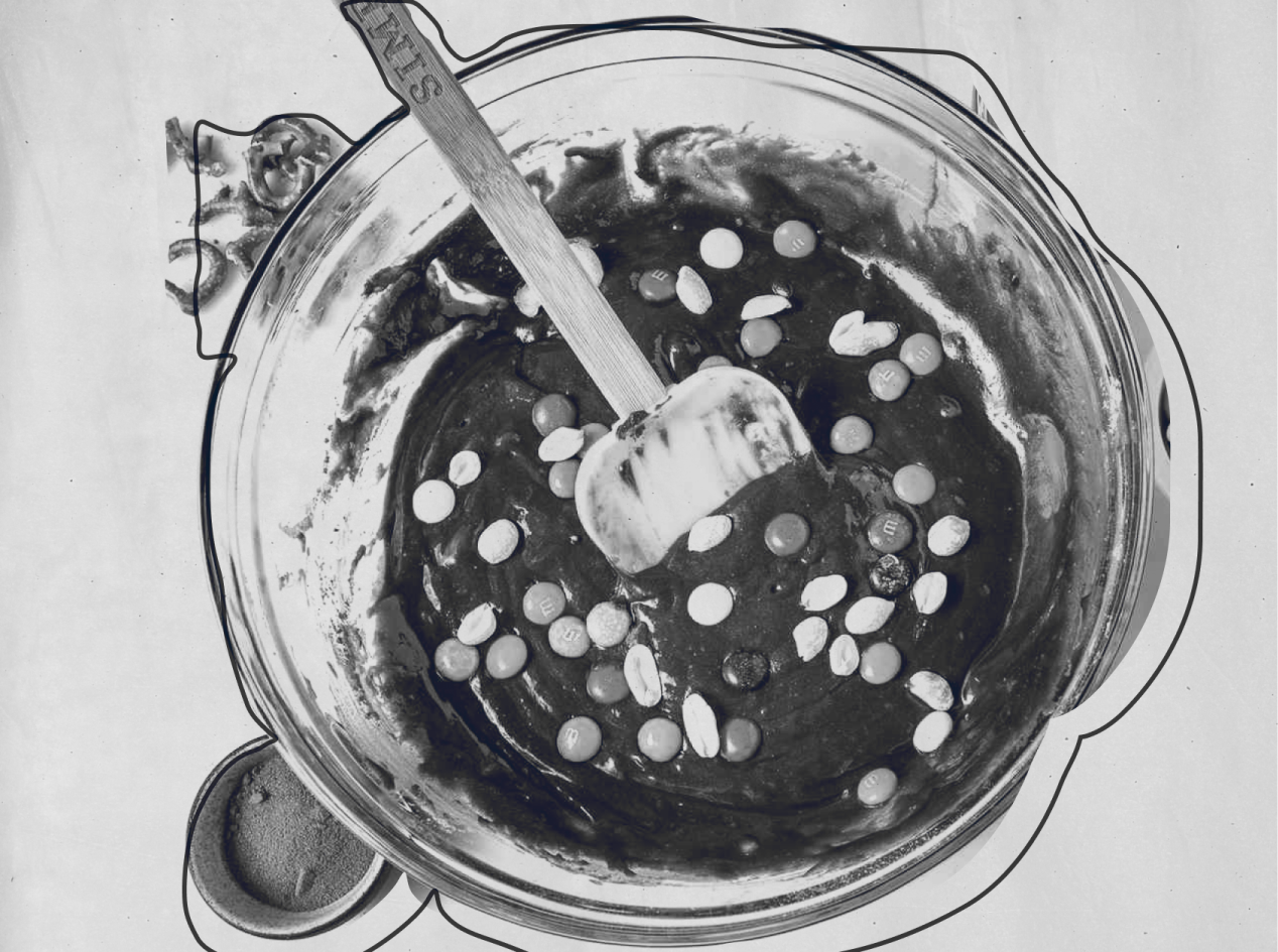 Mixing chocolate batter with peanuts and candy in a glass bowl with a spatula.