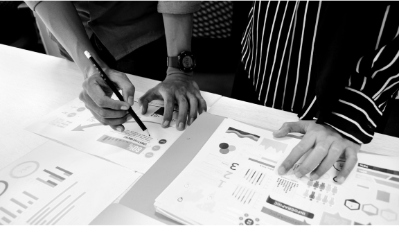 Two people are closely examining and pointing at printed charts and graphs on a desk, highlighting data analysis.