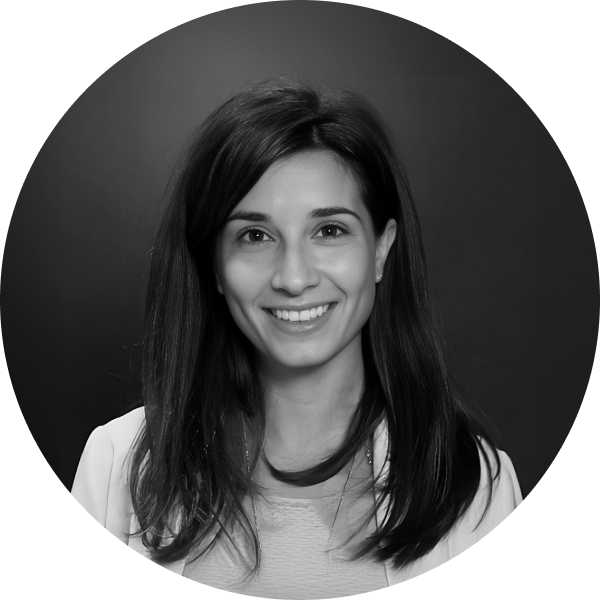 Black and white portrait of a woman with long, dark hair, smiling at the camera against a dark background. She is wearing a light-colored top and blazer, exuding confidence as if presenting expert monetization solutions.